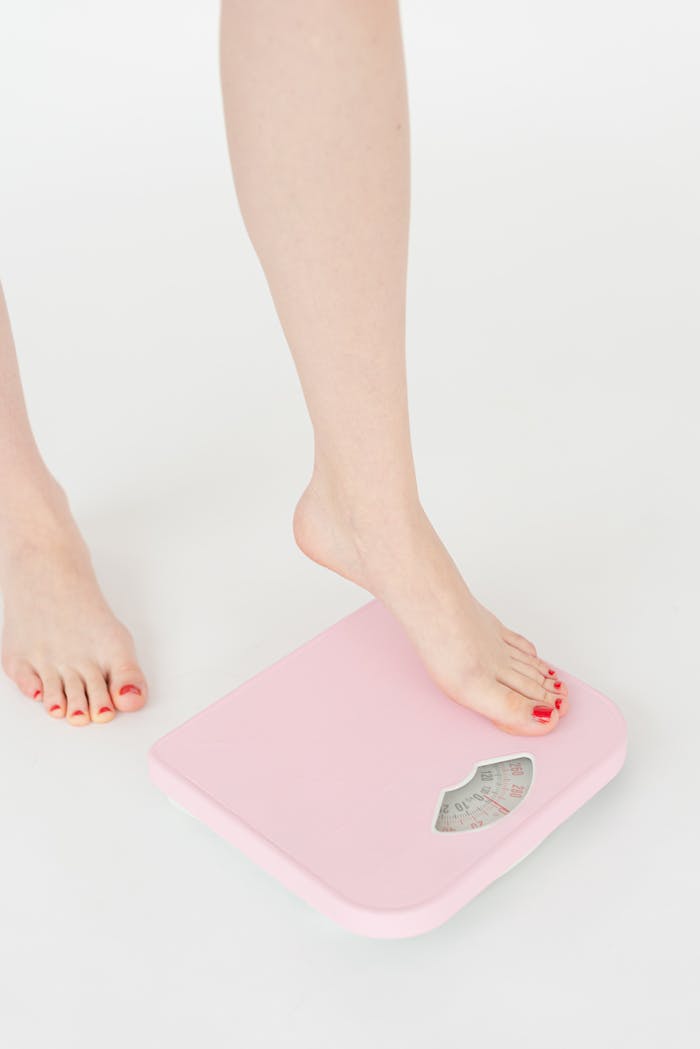 services-04 A woman's feet with red nails stepping onto a pink weight scale, symbolizing health and wellness.