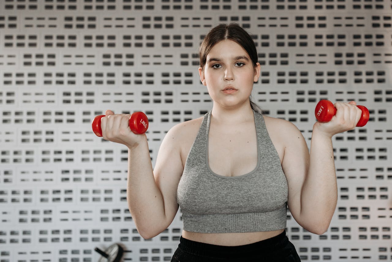 gallery-6 Confident woman exercising indoors with red dumbbells, focusing on strength training and fitness.