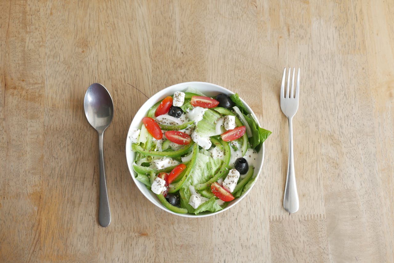 A fresh vegetable salad with feta cheese, olives, cherry tomatoes, and dressing, placed on a wooden table.